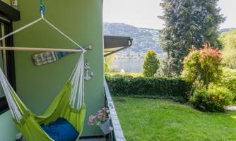 A hammock on a balcony overlooking a beautiful garden. In the background, trees and a landscape can be seen.