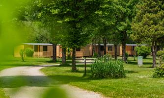 A tranquil landscape with wooden chalets, surrounded by green trees. A well-kept path leads through the garden.
