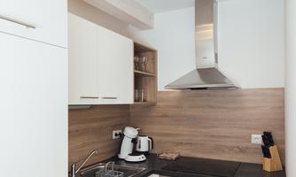 A modern kitchen with white cabinets and a dark countertop. The equipment includes a stove, a refrigerator, and a coffee machine.