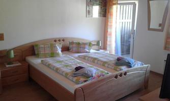 A cozy room with two single beds and colorful bedding. There are windows with curtains and a wooden dresser.