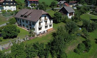 A beautiful house surrounded by lots of greenery and trees. In the background, other buildings can be seen.