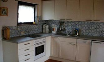 A modern kitchen with white cabinets and a blue tile backsplash. There are cooking appliances and a sink available.