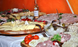 A lavish selection of sausages, cheese, and fresh vegetables on a table. There is also a bottle of drink and decorative side dishes.