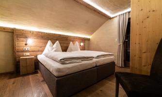 A cozy bedroom with a double bed and wooden paneling. Soft lighting and a windowsill create a relaxed atmosphere.