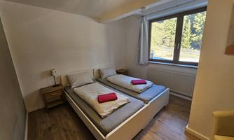 A simple bedroom with two single beds and red towels. The window offers a view of the outdoors.