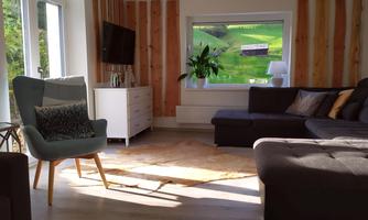 A modern living room with a comfortable sofa and a nice armchair. Large windows offer a view of the green landscape outside.