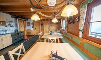 A cozy kitchen with wooden furniture and a large dining table. Bright lamps and traditional decorations give the room an inviting atmosphere.