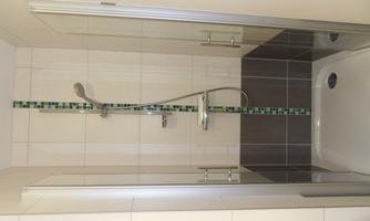 A modern shower with glass walls and a simple, tiled design. The shower is equipped with a stylish mixer tap.