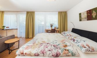 A bright bedroom with a large bed and colorful blankets.  
Next to the bed is a cozy sitting area and a table with chairs.