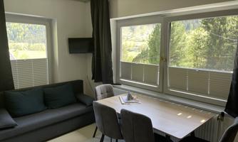 A modern living room with a comfortable sofa and a dining table. Large windows let in plenty of light and offer a view of the nature outside.