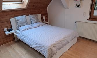 A cozy bedroom with a white bed and decorative pillows. The wood paneling and a window create a warm atmosphere.