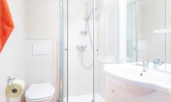 A modern bathroom with a shower cabin and bright colors. Orange towels and a bathroom rug add a fresh touch.