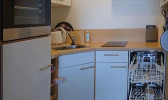 A modern kitchen with white cabinets and a built-in oven. The dishwasher is open and ready for dishes.