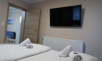 A modern room with two beds, a television, and a wooden wardrobe. The walls are painted in neutral colors, and the lighting is friendly and welcoming.