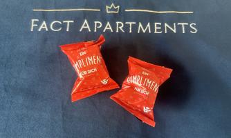 Two red chocolate packages with the inscription "A compliment for you" are lying on a blue table with the "Fact Apartments" logo. They are a friendly welcome gift for guests.