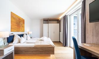 A modern hotel room with a large bed and stylish design. The room has large windows that let in a lot of light.