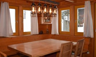 A cozy dining area in a wooden cabin with large windows and warm light. The table is made of wood and accommodates several people.