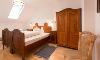 A cozy bedroom with two beds and wooden furniture. A round rug and a chair complete the decor.