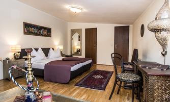 A modern room with a large bed and decorative elements. A hookah and an elegant table complement the furnishings.