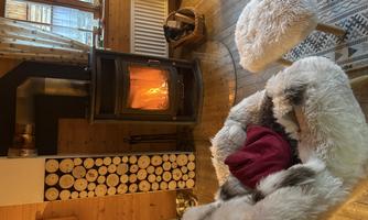 A cozy living space with a fireplace and a comfortable armchair. Firewood is neatly stacked, creating a warm atmosphere.