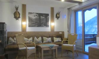 A cozy lounge with wooden paneling and a comfortable couch. Large windows offer a view of the mountains.