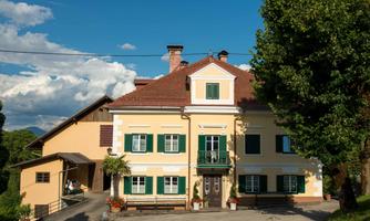 A charming house with a yellow facade and green windows, surrounded by trees. A clear blue sky completes the picturesque scene.