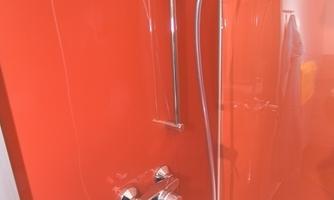 A modern shower with shiny fixtures against a bright red wall. The elegant showerhead adds to a stylish bathroom decor.