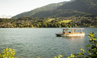 A small boat is floating on a clear lake, surrounded by green mountains and an idyllic landscape. The scene radiates tranquility and a connection to nature.