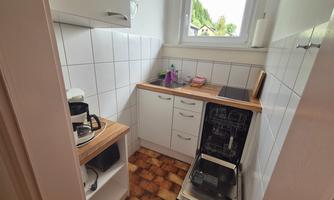 A small kitchen with white tiles and wood details. On the countertop, there is a coffee machine and a dishwasher.