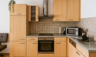 A modern kitchen with wood cabinets and a granite countertop. It is equipped with an oven, a refrigerator, and a microwave.