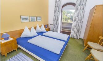 A cozy bedroom with two beds and white pillows. Large windows provide a view of the surroundings.