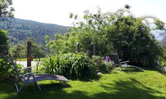 A quiet garden with two deck chairs on green grass. In the background, trees and hills can be seen.