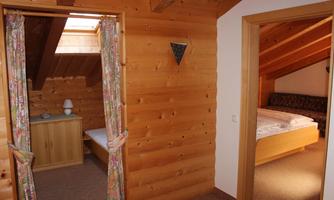 A cozy wooden room with a skylight and two bedrooms. The walls are made of wood and there are windows with natural light.