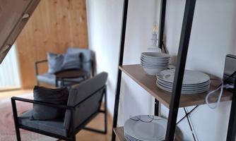 A cozy living area with a modern shelf and dishes. In the background, there is a comfortable armchair on a hardwood floor.