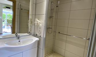 A modern bathroom with a shower, sink, and large tiles. The lighting is bright and friendly.