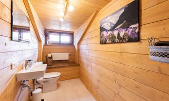 A modern bathroom with wooden walls and a large window. It includes a sink, a toilet, and a decorative picture on the wall.
