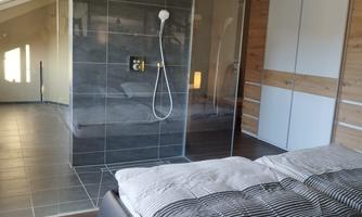 A modern bedroom with a large double bed and an elegant glass shower. The walls are designed in dark and light tones, giving it a stylish look.