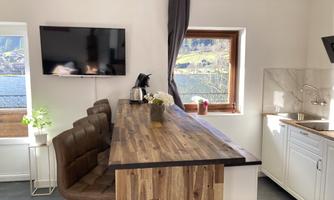 A modern kitchen with a wooden bar and cozy chairs. The windows offer a beautiful view of the landscape.