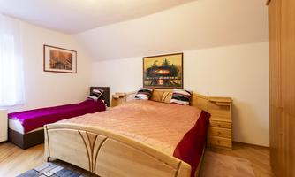A cozy bedroom with a large bed and a single bed. The walls are decorated with pictures and there is a wooden wardrobe.