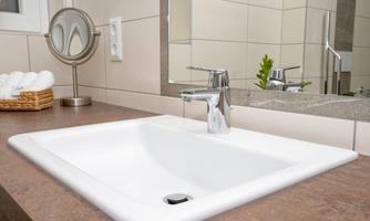 A modern sink on a brown countertop. In the background, mirrors and decorative elements can be seen.