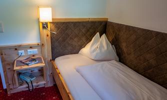 A cozy single room with wooden paneling and a large bed. Next to the bed is a nightstand with a lamp and a telephone.