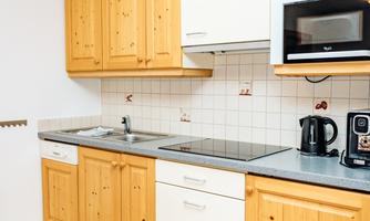 A modern kitchen with wooden cabinets and white fronts. The equipment includes a stove, a microwave, and a kettle.