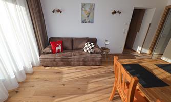 A modern living room with a brown sofa and a wooden table. Large windows let in a lot of light.