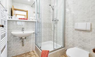 A modern bathroom with a shower cubicle, a sink, and a toilet. The walls are light tiled and there is a towel in orange.