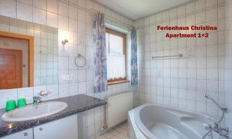 A bright bathroom with modern tiles and an elegant bathtub. The sink is placed next to a large window front and offers plenty of space.