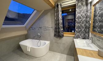 An elegant bathroom with a freestanding bathtub and modern sinks. Large windows provide bright lighting and a cozy atmosphere.