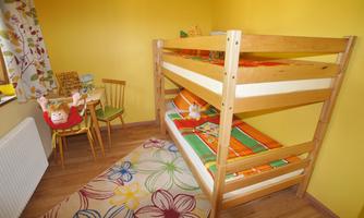 A brightly designed children's room with a bunk bed and a small sitting area. The walls are painted yellow, and a carpet with a floral pattern lies on the floor.