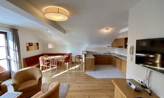 A bright, modern living room with cozy furniture and an open kitchen. Large windows provide plenty of daylight.