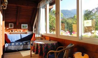 A cozy room with wooden walls and plenty of daylight. A table and chairs invite relaxation, while the view of the mountains is visible.