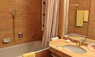 An elegant bathroom with a bathtub and a marble sink area. The walls are lined with warm beige tiles and two yellow towels are hanging.